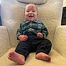 Kayson is registered to the contest to win money with this photo: baby, smiling, child, infant, plaid_shirt, black_pants, barefoot, armchair, cozy, indoor, happy, portrait, cute, small_hands, feet, red_mark, comfortable, seated, furniture, person