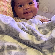 Zorah is registered to the contest to win money with this photo: baby, smiling, blanket, heart_pattern, cushioned_chair, animal_print, face, happy, cozy, indoor, child, infant, soft_texture, cute, person, portrait, wrapped, warm, young, resting