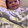baby, smiling, blanket, heart_pattern, cushioned_chair, animal_print, face, happy, cozy, indoor, child, infant, soft_texture, cute, person, portrait, wrapped, warm, young, resting