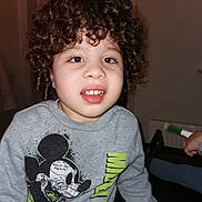 Zayne is registered to the contest to win money with this photo: child, curly_hair, sweatshirt, mickey_mouse, indoor, portrait, face, smile, casual_clothing, person, young, kid, cute, light_skin, sitting, window, home, furniture, toy, hand