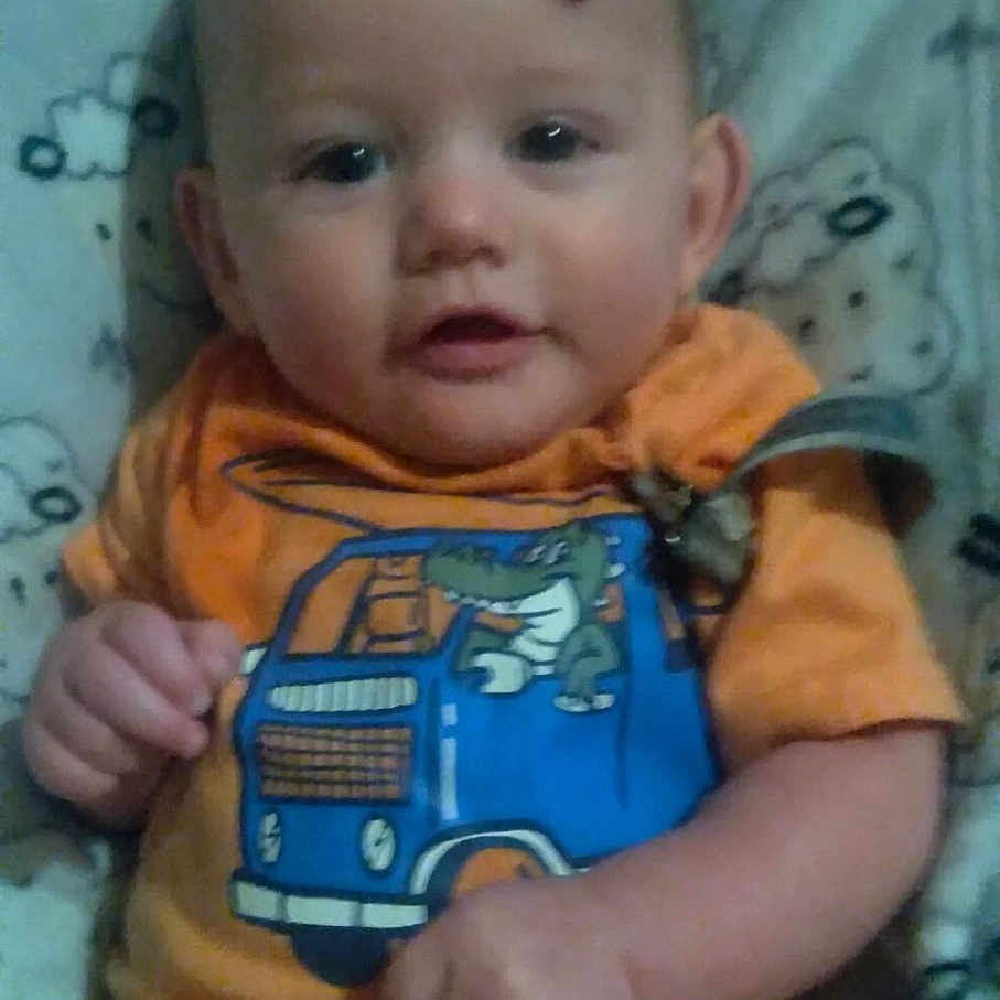 Adam joined the competition — help win amazing prizes! baby, blanket, blue_truck, child, cloud_pattern, crocodile_design, cute, face, hands, head, indoors, infant, legs, onesie, orange_clothing, person, portrait, sitting, skin_mark, young