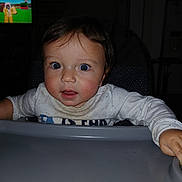 Jeremiah is registered to the contest to win money with this photo: baby, infant, child, high_chair, portrait, face, eyes, wide_eyed, sitting, indoor, home, dining_area, tray, shirt, sleeves, television, cartoon, dark_room, flash_photography, close_up