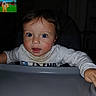baby, infant, child, high_chair, portrait, face, eyes, wide_eyed, sitting, indoor, home, dining_area, tray, shirt, sleeves, television, cartoon, dark_room, flash_photography, close_up