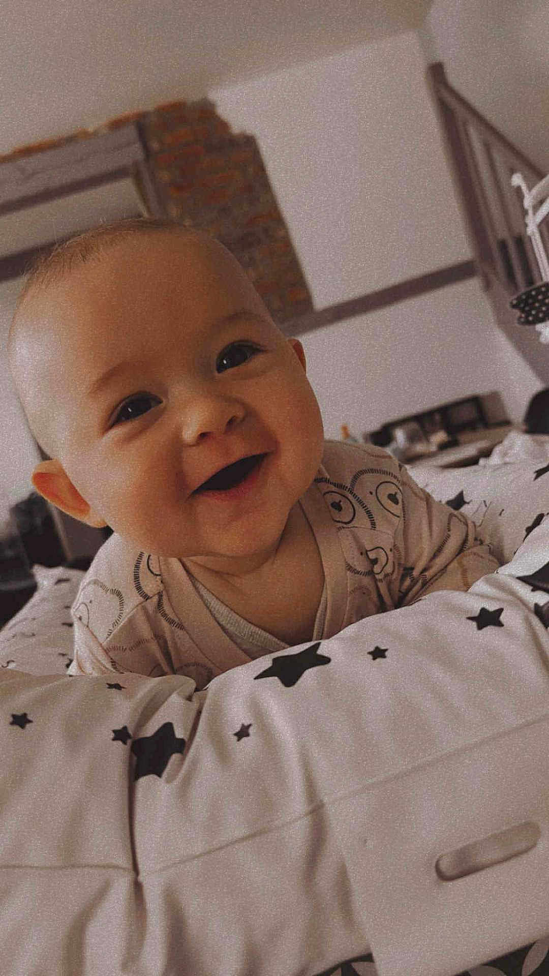 Elïo a rejoint le concours — aidez-le/la à gagner de superbes lots ! baby, smiling, infant, face, cute, star_pattern, cushion, indoor, child, happy, person, clothing, head, young, portrait, bedroom, cozy, cheeks, eyes, lying_down