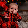 baby, infant, red_clothing, black_clothing, plaid_pattern, onesie, blanket, holiday_lights, christmas, blurred_background, cute, child, indoor, portrait, sitting, hand, face, head, soft_texture, cozy