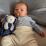 Sohan a rejoint le concours — aidez-le/la à gagner de superbes lots ! baby, pacifier, plush_toy, bunny, blue_clothing, cream_pants, cushion, soft_texture, indoor, infant, child, cute, lying_down, serious_expression, toy, comfort, cozy, face, person, home