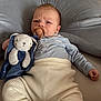 baby, pacifier, plush_toy, bunny, blue_clothing, cream_pants, cushion, soft_texture, indoor, infant, child, cute, lying_down, serious_expression, toy, comfort, cozy, face, person, home