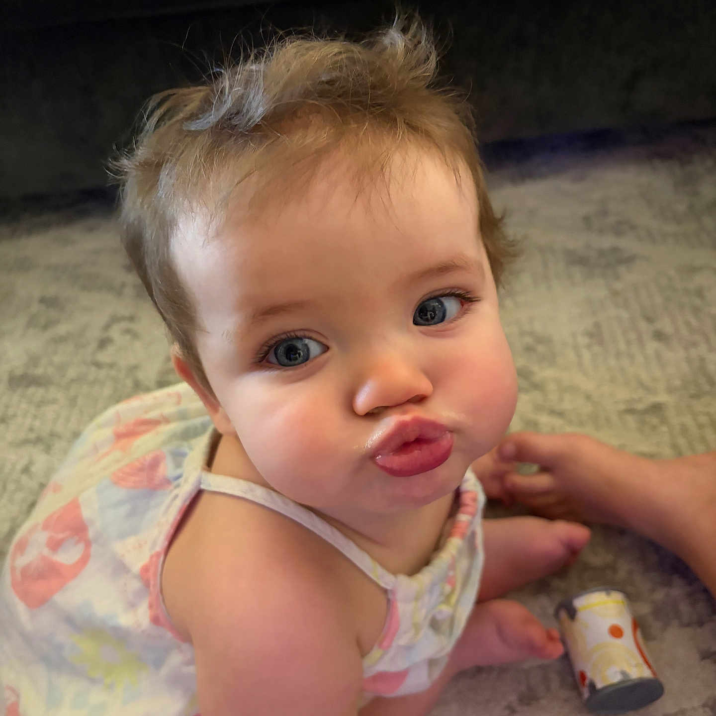 Madison is registered to the contest to win money with this photo: baby, child, cute, duck_face, blue_eyes, dress, carpet, toy, sitting, tousled_hair, puckered_lips, indoor, foot, playful, infant, person, portrait, skin, expression, closeup