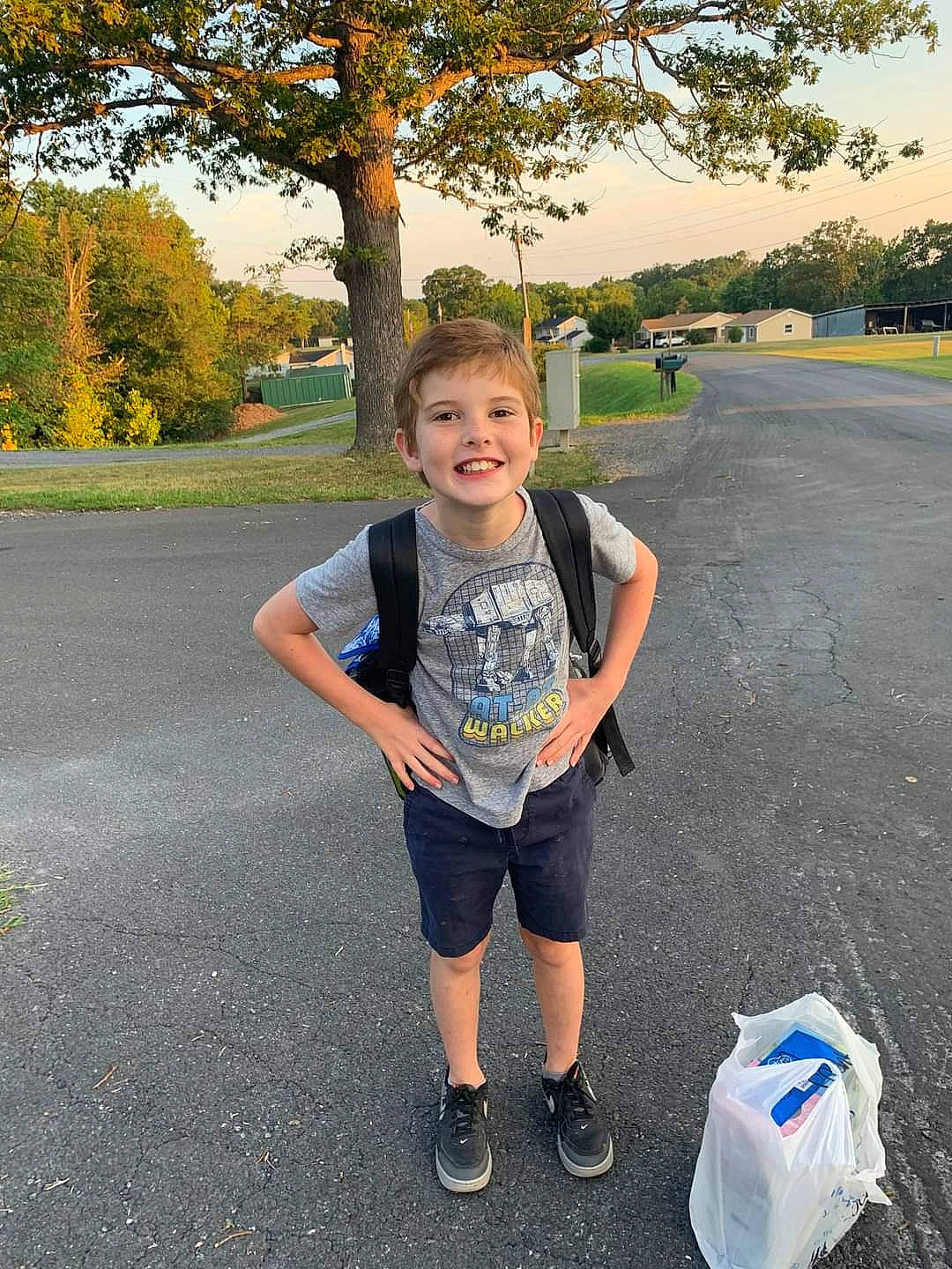 Hayden is registered to the contest to win money with this photo: asphalt, bag, electric_blue, fun, grass, happy, joy, leisure, luggage_and_bags, person, plant, public_space, recreation, road, road_surface, shorts, sky, smile, t_shirt, toddler