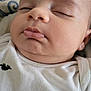 Brent is registered to the contest to win money with this photo: baby, sleeping, close_up, onesie, dinosaur_print, infant, face, peaceful, child, cute, soft_skin, resting, portrait, young, indoors, head, clothing, patterned_background, calm, small