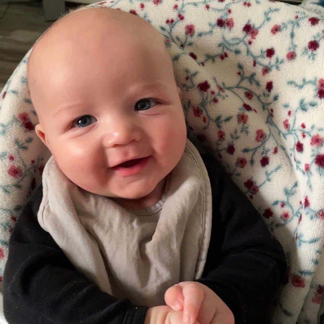 Elijah joined the competition — help win amazing prizes! baby, bib, blanket, child, clothing, cute, eyes, face, floral_pattern, hands, happy, head, high_chair, indoor, infant, mouth, person, portrait, skin, smiling