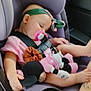 baby, car_seat, child, pacifier, plush_toy, sleeping, headband, pink_clothing, toy, car_interior, seatbelt, tattoo, infant, cute, relaxed, child_safety, baby_girl, comfort, nap, soft_toy
