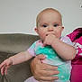 baby, child, infant, person, hand, face, couch, clothing, colorful, sitting, indoor, adult_hand, pink, pattern, heart, cute, cheeks, eyes, comfort, casual