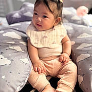Jillian is registered to the contest to win money with this photo: baby, child, infant, sitting, cushion, cloud_pattern, pastel_clothing, bib, hair_clips, indoor, soft_lighting, cozy, cute, feet, hands, face, expression, blurred_background, comfort, playful