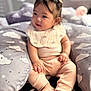 baby, child, infant, sitting, cushion, cloud_pattern, pastel_clothing, bib, hair_clips, indoor, soft_lighting, cozy, cute, feet, hands, face, expression, blurred_background, comfort, playful