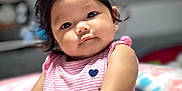 Jillian is registered to the contest to win money with this photo: baby, child, infant, portrait, pink_dress, striped_clothing, heart_emblem, curly_hair, soft_toys, cushion, indoors, cute, smiling, sitting, closeup, face, skin, hands, cozy, warm_lighting