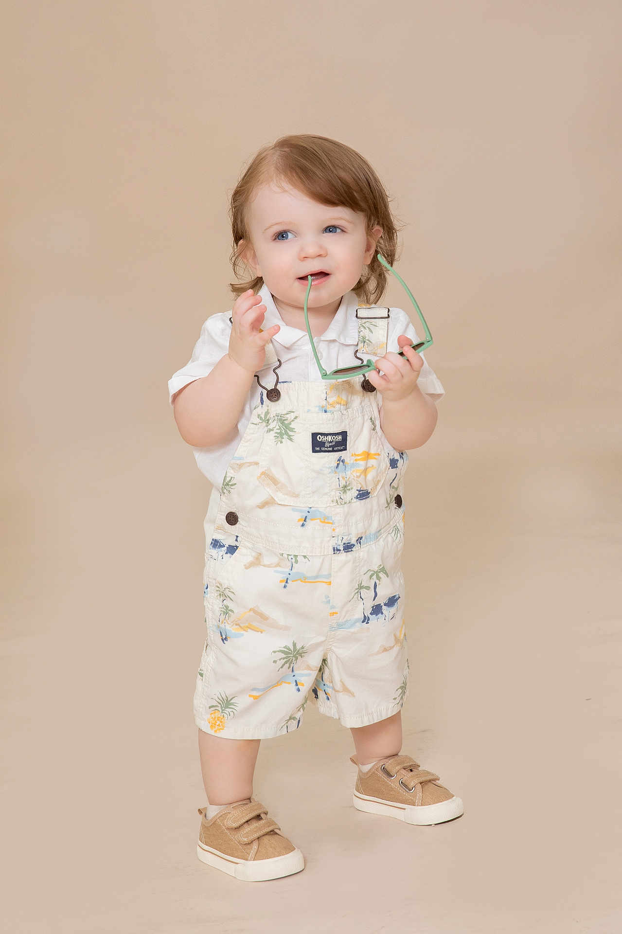 Archer is registered to the contest to win money with this photo: toddler, child, standing, sunglasses, overalls, white_shirt, beige_background, shoes, cute, playful, innocent, portrait, studio, fashion, young_child, smiling, short_hair, indoors, casual_clothing, person