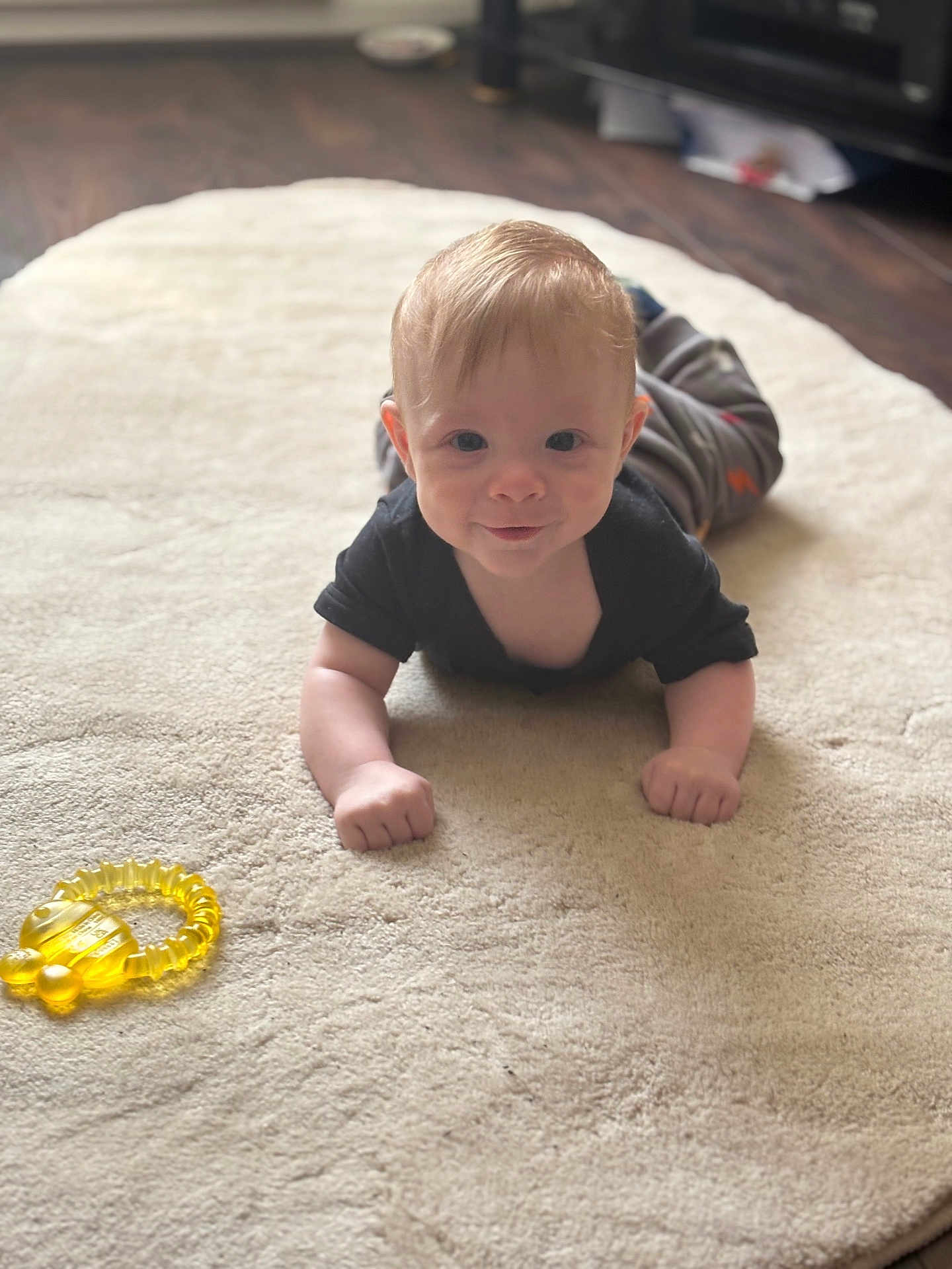 Brendon joined the competition — help win amazing prizes! baby, infant, carpet, toy, teething_ring, smile, black_shirt, gray_pants, indoor, floor, child, young, cute, lying_down, looking_at_camera, soft_lighting, cozy, home, person, playtime