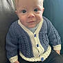 baby, child, face, knitwear, cardigan, blue, white, buttons, couch, cushion, clothing, sitting, portrait, indoor, person, smile, young, cute, cozy, casual