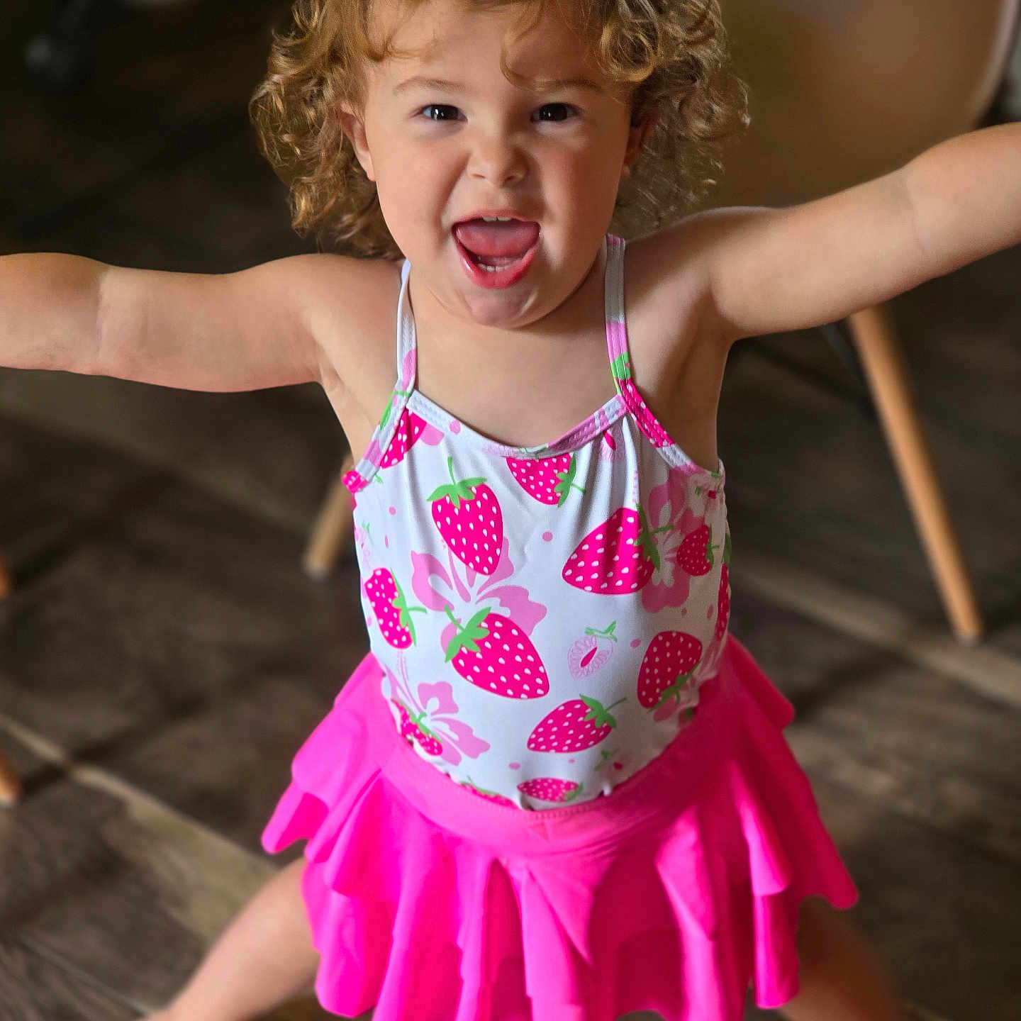 Kenzleeann Lucas joined the competition — help win amazing prizes! arms_outstretched, barefoot, bright_colors, chair, cheerful, child, curly_hair, cute, happy, indoor, person, pink_skirt, playful, portrait, short_sleeves, smiling, standing, strawberry_pattern, toddler, wooden_floor