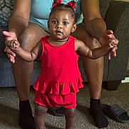 Endia is registered to the contest to win money with this photo: toddler, child, adult, red_outfit, sparkly_shoes, hair_bows, carpet, couch, living_room, person, holding_hands, smiling, indoor, furniture, legs, seated, cute, family, support, home