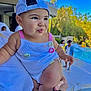 baby, child, cap, hat, knitted_outfit, blue_sky, pool, outdoor, sunny, greenery, adult_hand, puckered_lips, cute, chubby_cheeks, summer, people, blurred_background, playful_expression, daylight, holding