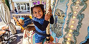Melyne Marie participe au concours pour gagner de l'argent avec cette photo : child, smiling, carousel, pig, amusement_ride, outdoor, daylight, braided_hair, blue_clothing, black_sleeves, white_shoes, vintage, decorative_lights, pastoral_painting, urban_background, window, building, wooden_floor, fun, playful