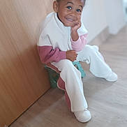 Melyne Marie a rejoint le concours — aidez-le/la à gagner de superbes lots ! blurred_background, casual_clothing, child, curly_hair, floor, flooring, happy, home, indoor, light, person, playful, portrait, relaxed, seated, smiling, stool, white_shoes, wooden_door, young_child