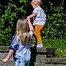 Vanessa is registered to the contest to win money with this photo: child, children, outdoor, nature, greenery, holding_hands, standing, stone_wall, sunlight, grass, helping, balancing, yellow_pants, tie_dye_shirt, person, playing, daytime, casual_clothing, friendship, support