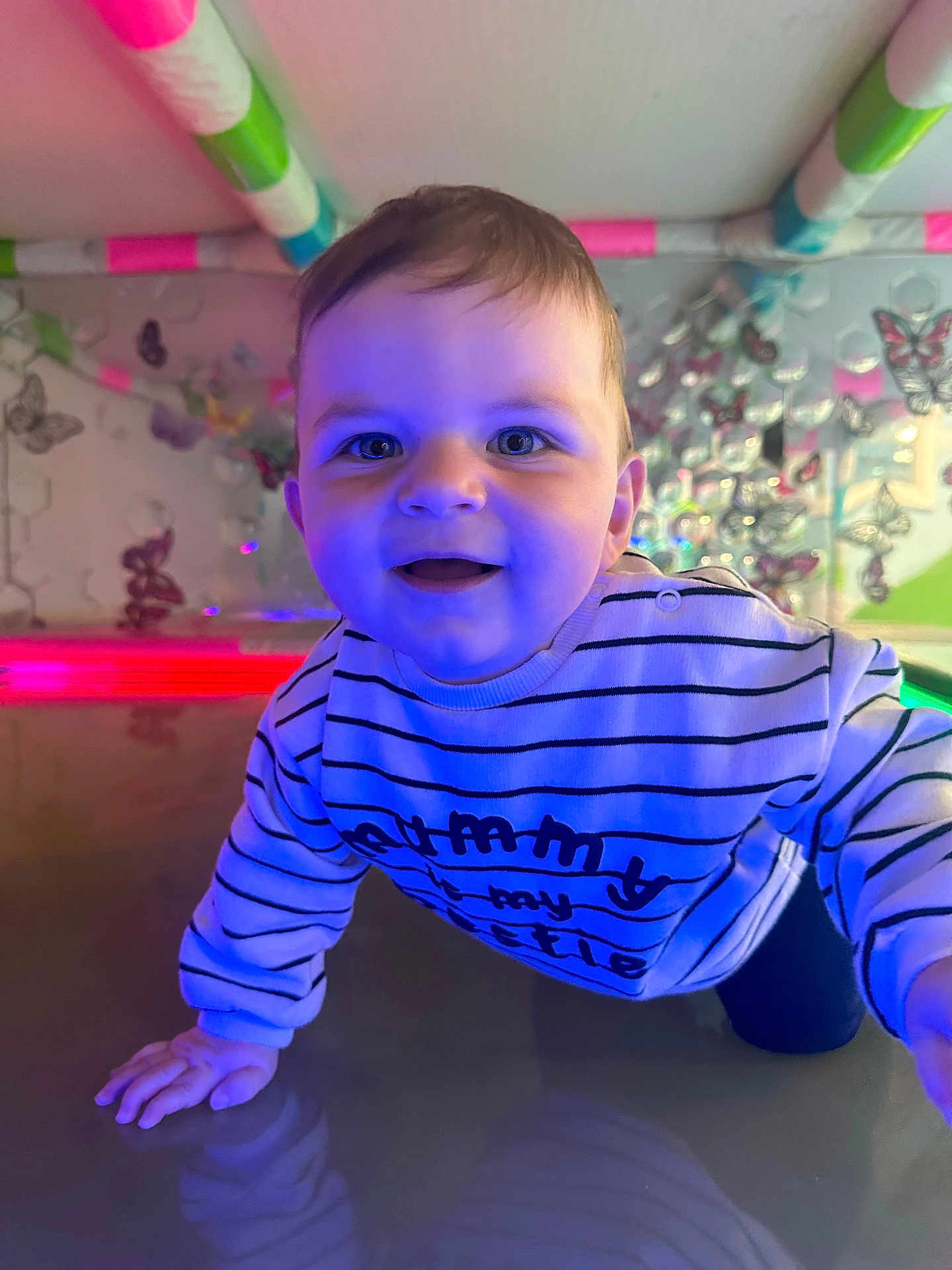 Finley joined the competition — help win amazing prizes! baby, child, crawling, smiling, blue_light, striped_shirt, indoor, butterfly_decor, colorful, happy, playful, cheerful, young_child, closeup, face, hand, reflection, decorations, cute, portrait