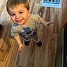 Eloy is registered to the contest to win money with this photo: child, boy, toddler, smiling, happy, portrait, indoors, wood_floor, toy, colorful_toy, educational_poster, short_hair, gray_shirt, cartoon_shirt, socks, standing, reaching, home, playroom, photography