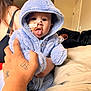 baby, blanket, blue_clothing, child, couch, cute, expression, face, hand, home, hood, hoodie, indoor, infant, person, playful, seated, soft_texture, tattoo, tongue_out