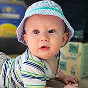 Everett joined the competition — help win amazing prizes! baby, child, infant, hat, striped_clothing, toddler, lying_down, indoor, curious, drool, face, hands, blue, green, white, candid, portrait, soft_light, young_child, casual_clothing