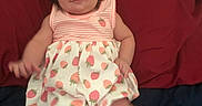 Isabela is registered to the contest to win money with this photo: baby, blanket, blue, child, clothing, couch, cute, dress, girl, hair, indoor, infant, person, ponytail, portrait, red, sitting, smile, strawberry_pattern, young