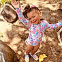 child, smiling, outdoor, sunlight, rocks, dirt, swimsuit, floral_pattern, shoes, play, happy, waving, toy_shovel, toy_mold, nature, summer, cute, playground, person, sand