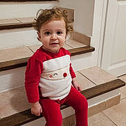 Magda participe au concours pour gagner de l'argent avec cette photo : child, cozy, curly_hair, cute, festive, happy, holiday, home, indoor, person, portrait, red_clothing, santa_outfit, sitting, smile, stairs, tile_floor, toddler, wooden_stairs, young_child
