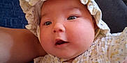 Nahanni joined the competition — help win amazing prizes! baby, infant, face, bonnet, clothing, button, couch, blue_cushion, indoor, closeup, skin, cheeks, eyes, person, child, cute, soft_texture, ruffle, sitting, portrait
