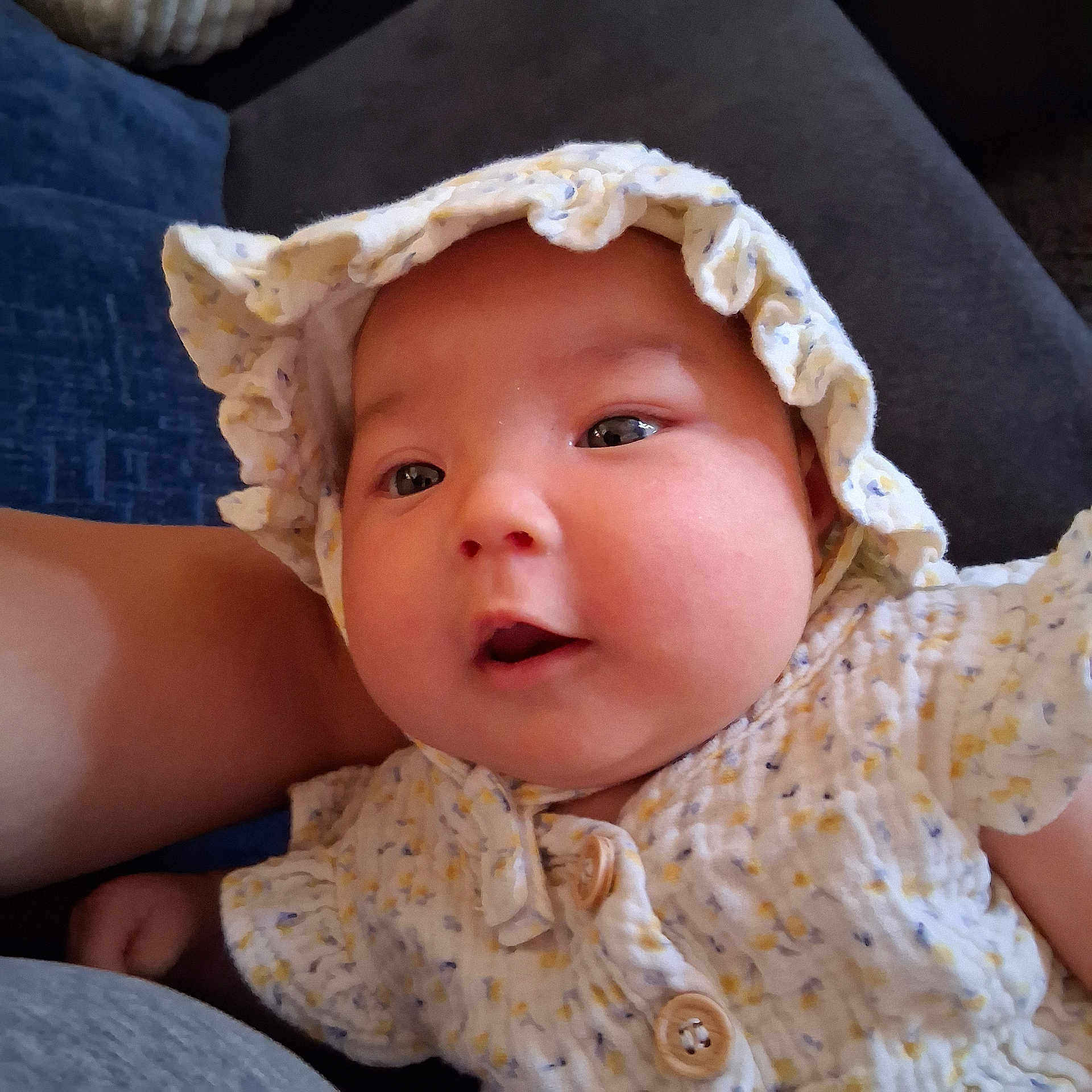 Nahanni joined the competition — help win amazing prizes! baby, infant, face, bonnet, clothing, button, couch, blue_cushion, indoor, closeup, skin, cheeks, eyes, person, child, cute, soft_texture, ruffle, sitting, portrait