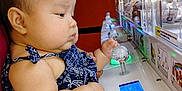 Nahanni is registered to the contest to win money with this photo: baby, child, claw_machine, arcade, toy, game, playing, lights, hand, adult, indoor, focus, patterned_clothing, cute, chubby_cheeks, serious_expression, seat, holding, entertainment, technology