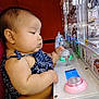 baby, child, claw_machine, arcade, toy, game, playing, lights, hand, adult, indoor, focus, patterned_clothing, cute, chubby_cheeks, serious_expression, seat, holding, entertainment, technology