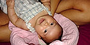 Nahanni is registered to the contest to win money with this photo: baby, infant, person, braid, gray_tank_top, pink_blanket, smile, skin, arm, hand, indoor, bed, clothing, face, happy, lying_down, holding, cute, young_child, cozy