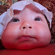 Nahanni is registered to the contest to win money with this photo: baby, face, close_up, chubby_cheeks, headwear, curious_expression, infant, skin, portrait, indoors, fabric_background, patterned, soft_lighting, child, cute, young, person, human, head, wearing