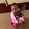 Jaya is registered to the contest to win money with this photo: baby, baby_walker, barefoot, blanket, brown_skin, child, curious, curly_hair, family, floor, hand, handle, indoor, looking_at_camera, pink, portrait, sitting, toddler, toy, wall