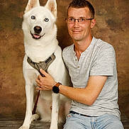 Rex participe au concours pour gagner de l'argent avec cette photo : animal_photography, backdrop, casual_clothing, companion, dog, glasses, harness, human, indoors, leash, man, pet_owner, portrait, sitting, smiling, standing_dog, studio, watch, white_dog, wood_floor