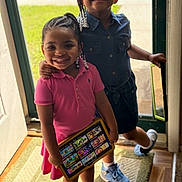 Kori is registered to the contest to win money with this photo: child, girl, smiling, braided_hair, beads, tablet, cartoon, doorway, sunlight, indoor, dress, sneakers, carpet, happy, family, technology, play, portrait, sibling, casual