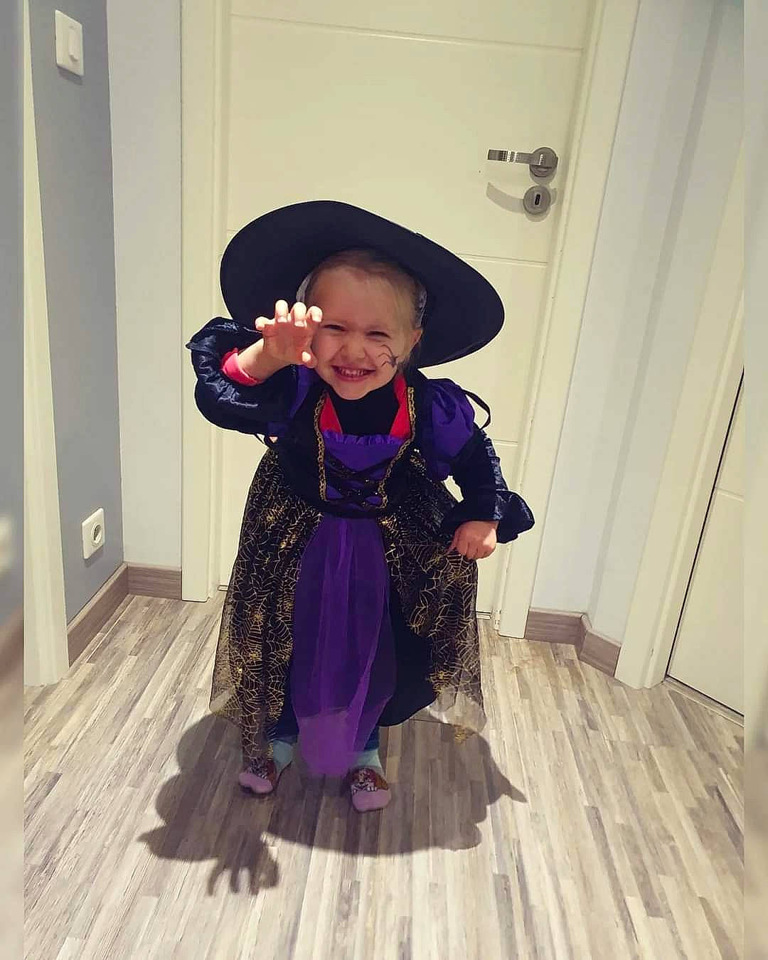 Lisa participe au concours pour gagner de l'argent avec cette photo : baby_toddler_clothing, costume_hat, door, dress, floor, flooring, formal_wear, fun, hardwood, hat, joy, magenta, person, purple, sleeve, smile, sun_hat, toddler, violet, witch_hat