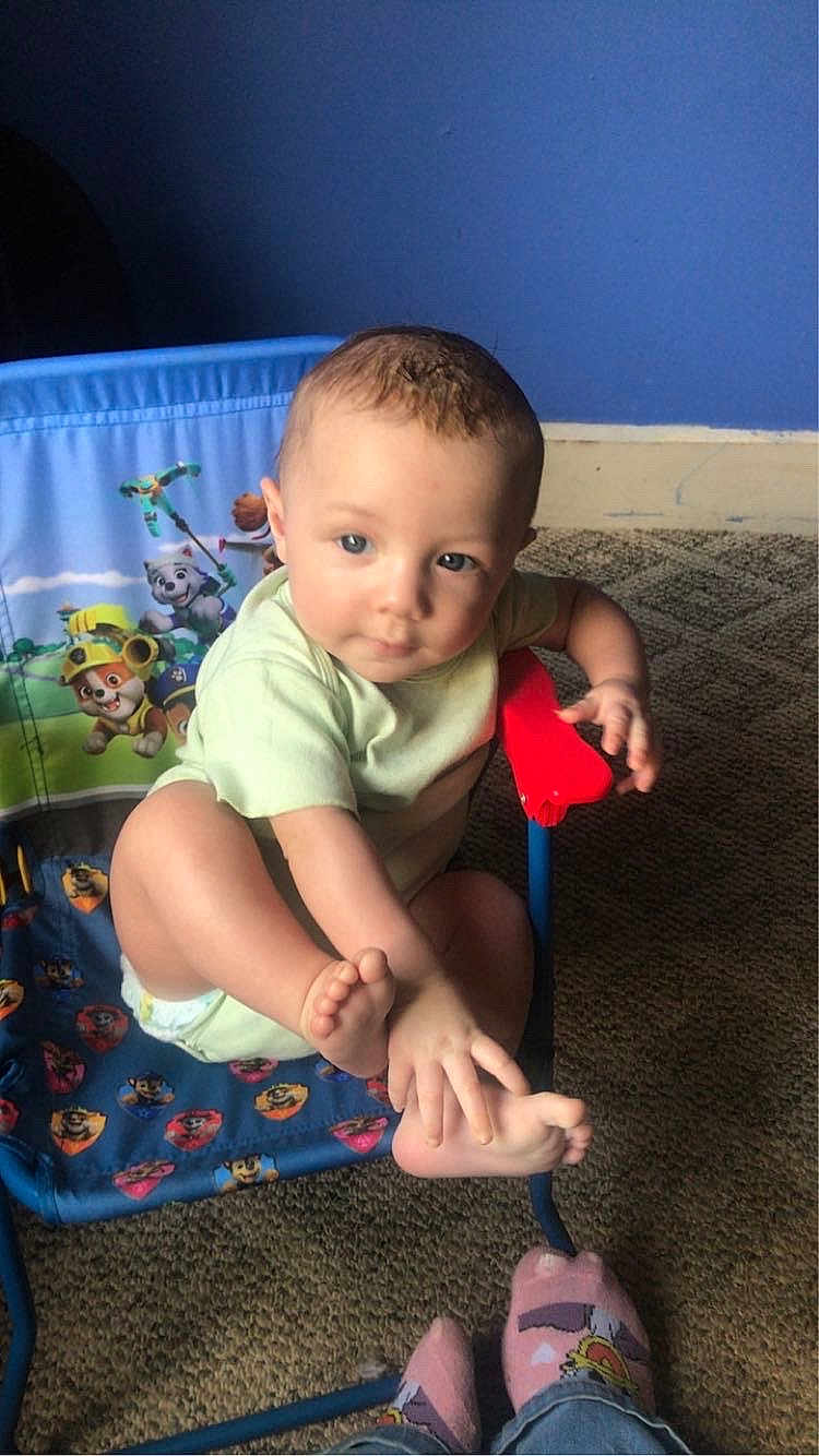 Otis is registered to the contest to win money with this photo: toddler, child, baby, chair, paw_patrol, foot, hand, indoor, carpet, blue_wall, socks, playing, curious, cute, clothing, person, furniture, toy_chair, casual, young_child