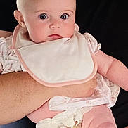 Katie is registered to the contest to win money with this photo: baby, infant, bib, person, arm, clothing, holding, face, skin, adult, black_shirt, pink_clothing, diaper, expression, indoor, closeup, cute, human, portrait, parent
