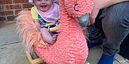 Katie is registered to the contest to win money with this photo: baby, child, rocking_toy, flamingo, pink, hat, bib, smiling, outdoor, patio, brick_wall, adult, jeans, blue_socks, grass, toy, happy, playful, person, footwear
