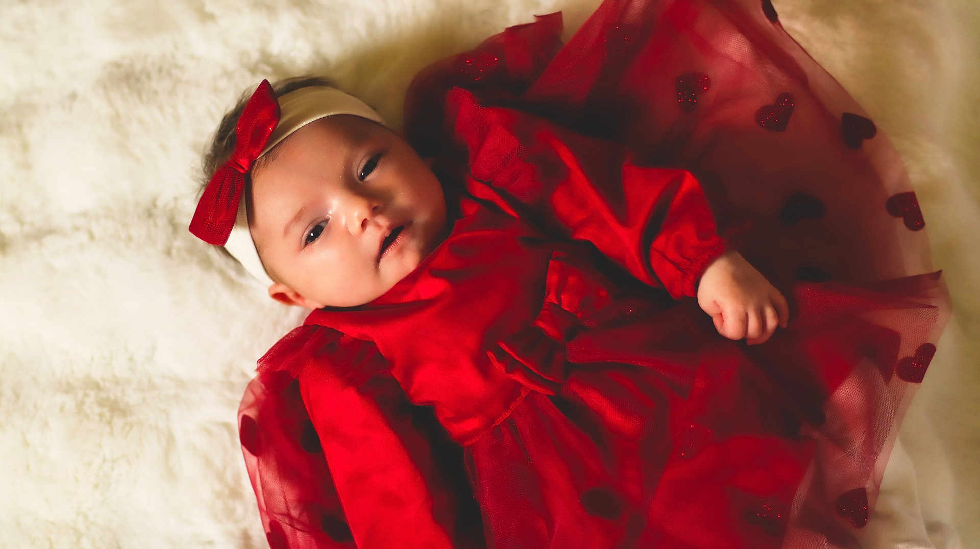 élyna a rejoint le concours — aidez-le/la à gagner de superbes lots ! baby, infant, red_dress, headband, bow, heart_pattern, blanket, soft_texture, portrait, lying_down, cute, child, young, indoors, fabric, clothing, face, hand, skin, adorable